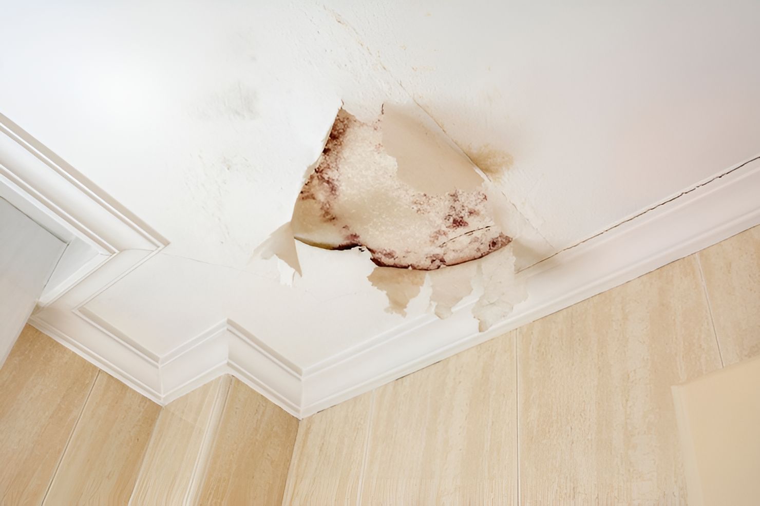 Water stain and peeling plaster on a white ceiling corner above beige walls
