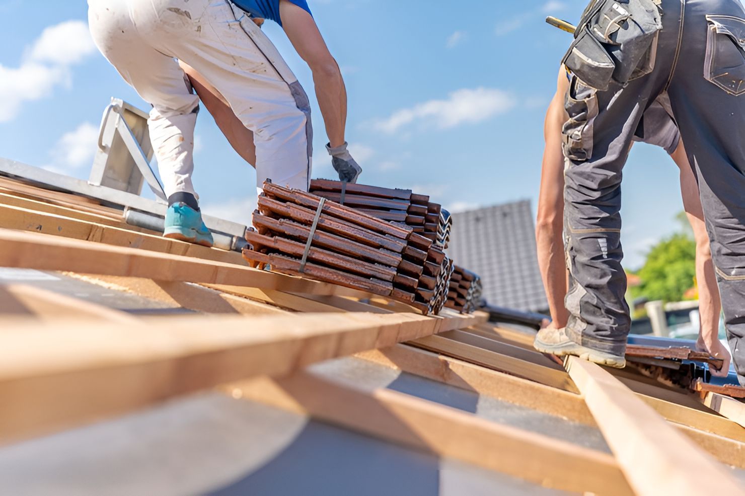 Workers installing roof tiles on a house roof under a blue sky