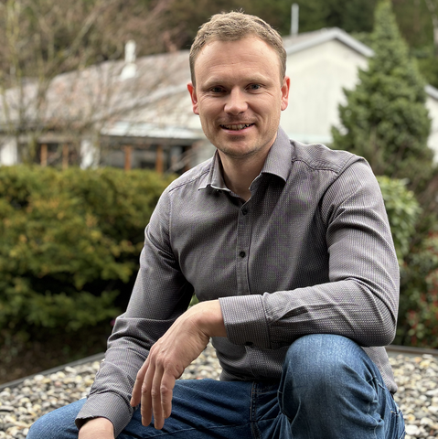 Ein Mann in einem grauen Hemd und blauen Jeans kniet auf einem felsigen Untergrund.