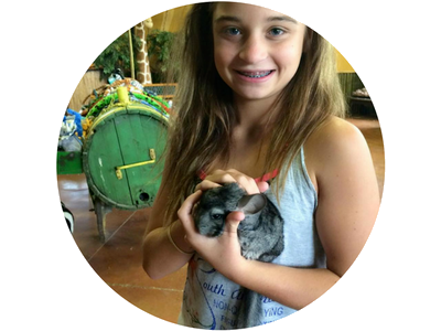 Smiling girl holding a gray chinchilla indoors, with a green barrel in the background