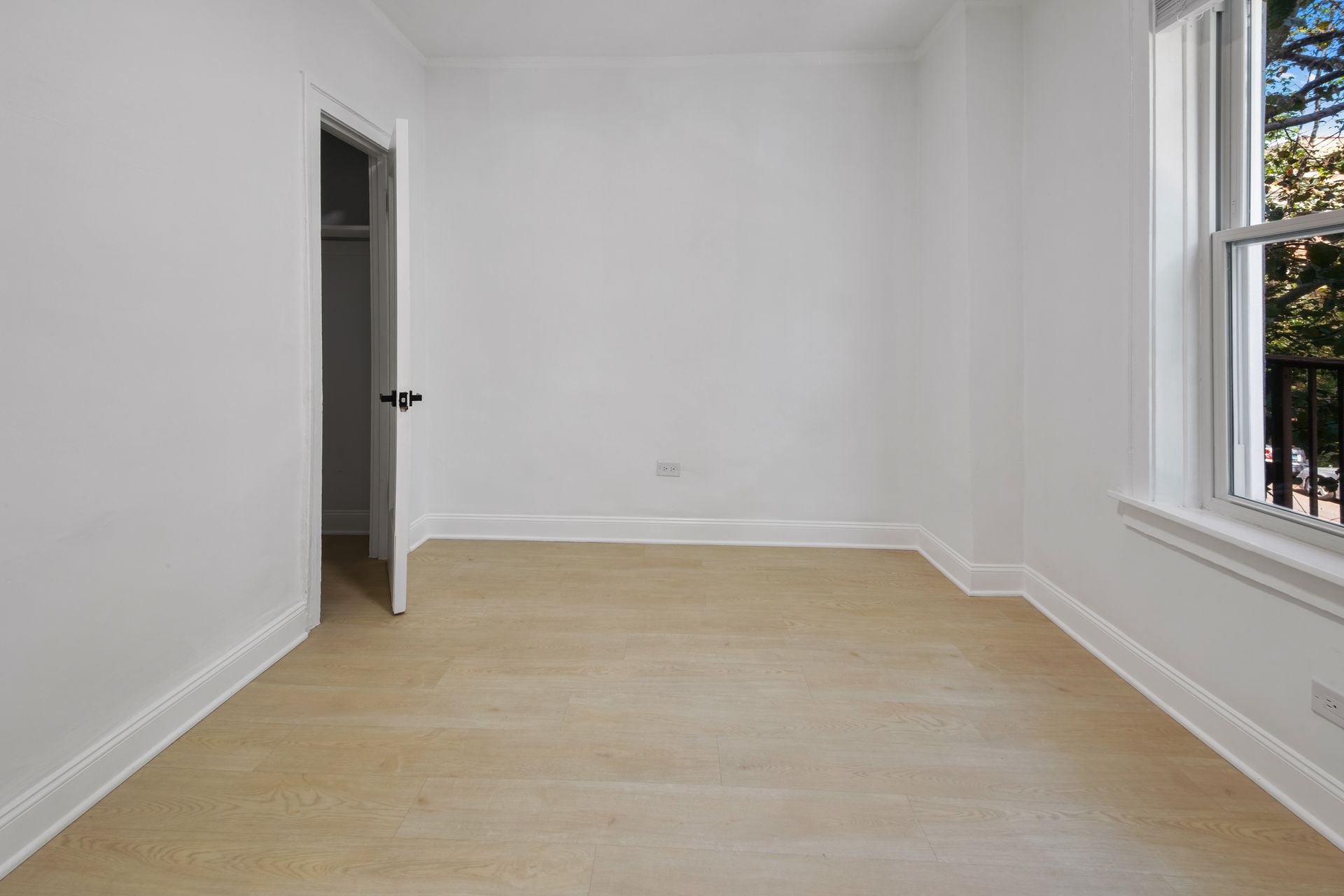 Empty white bedroom with light wood floor and a window.