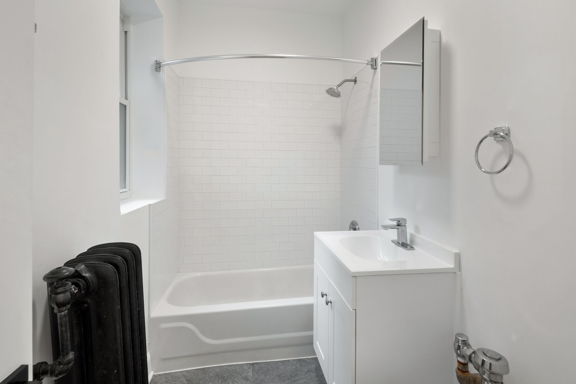 White bathroom with a bathtub, sink, and black radiator.