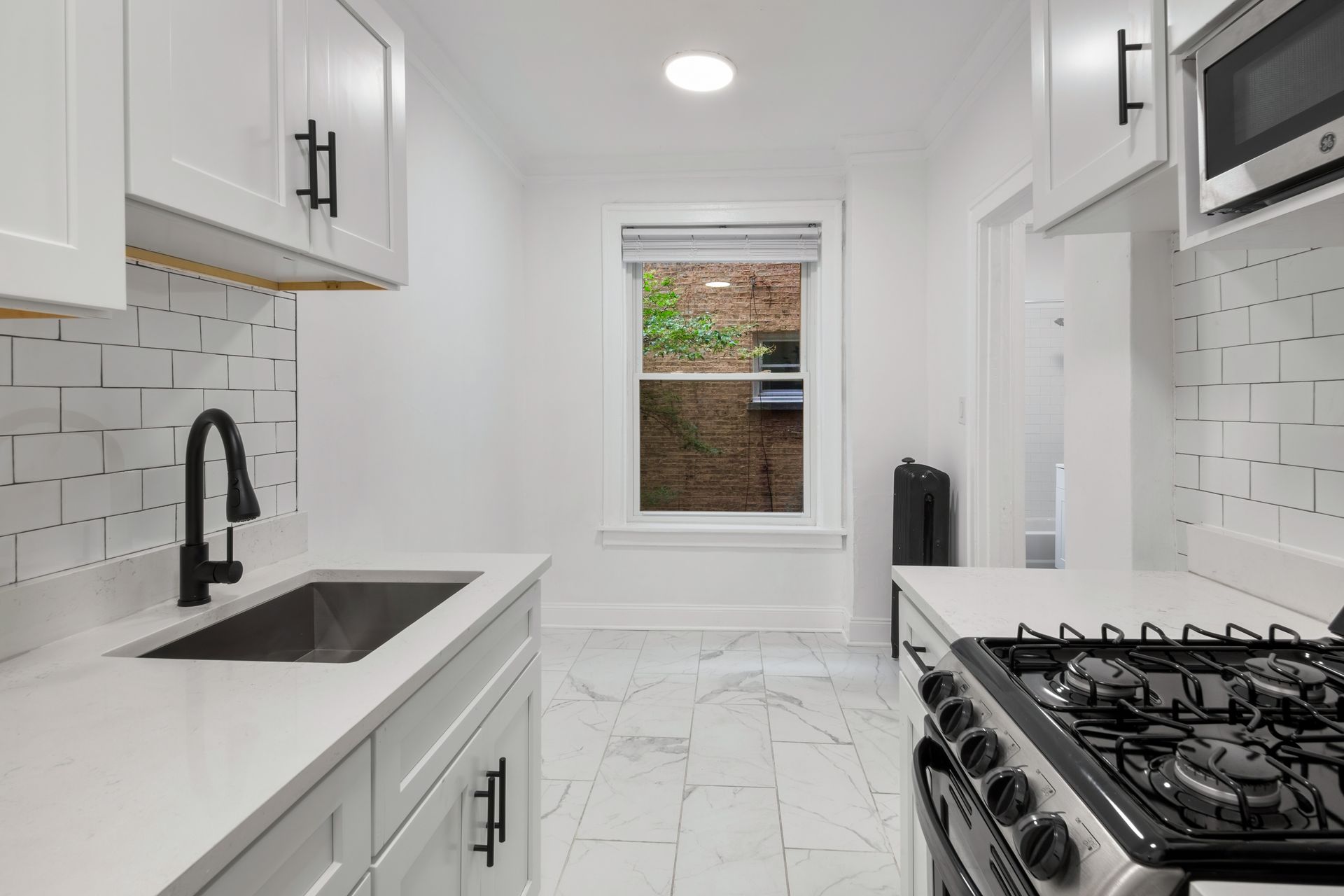 White kitchen with black accents: cabinets, sink, and range. Window views outside.