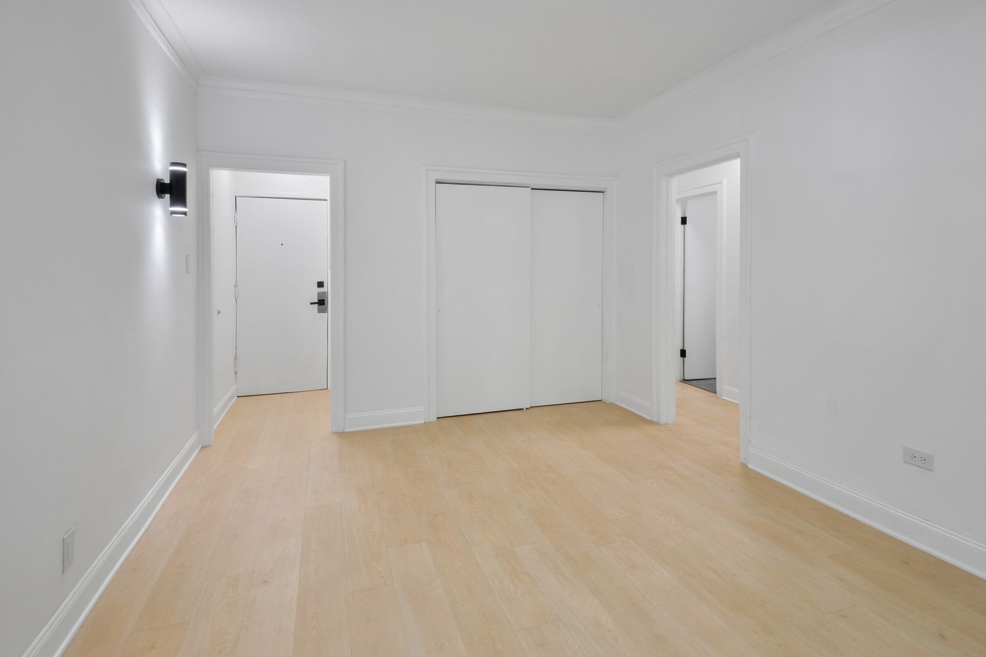 Empty room with light wood floor, white walls, closet, and doors.
