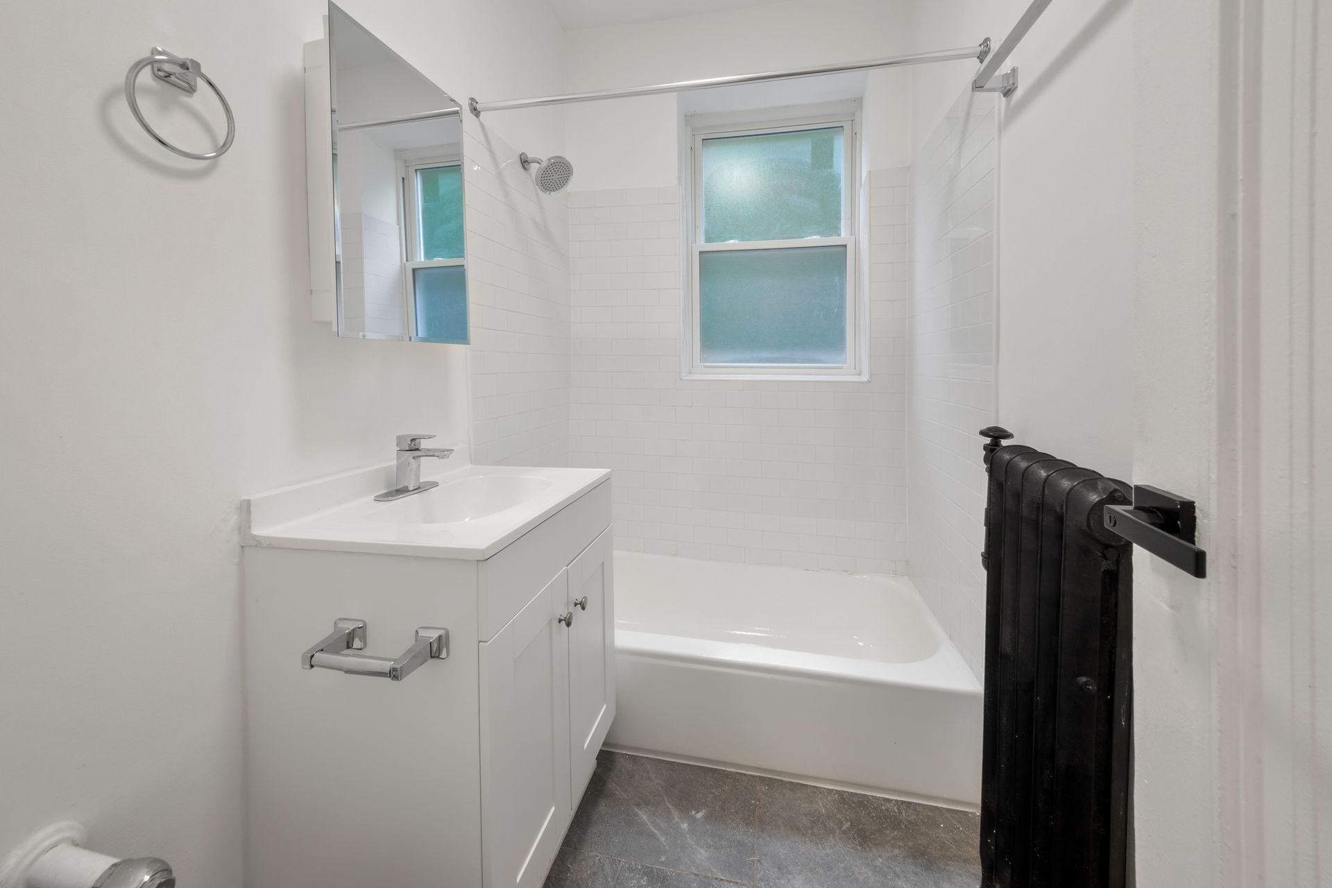 White bathroom with a vanity, tub, and window, with a dark towel rack.