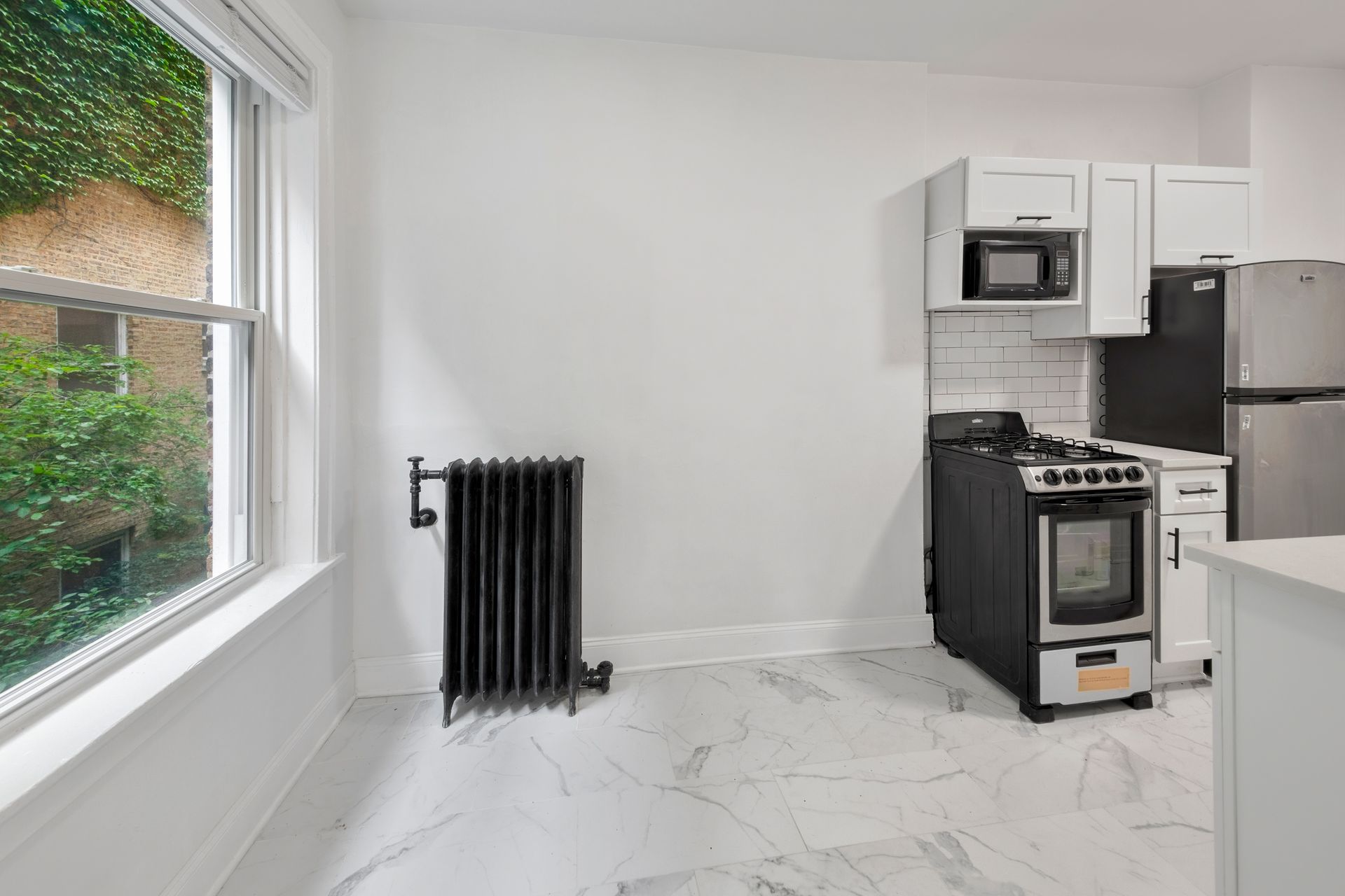 Kitchen with white cabinets, stainless steel appliances, a window with ivy, and a black radiator.