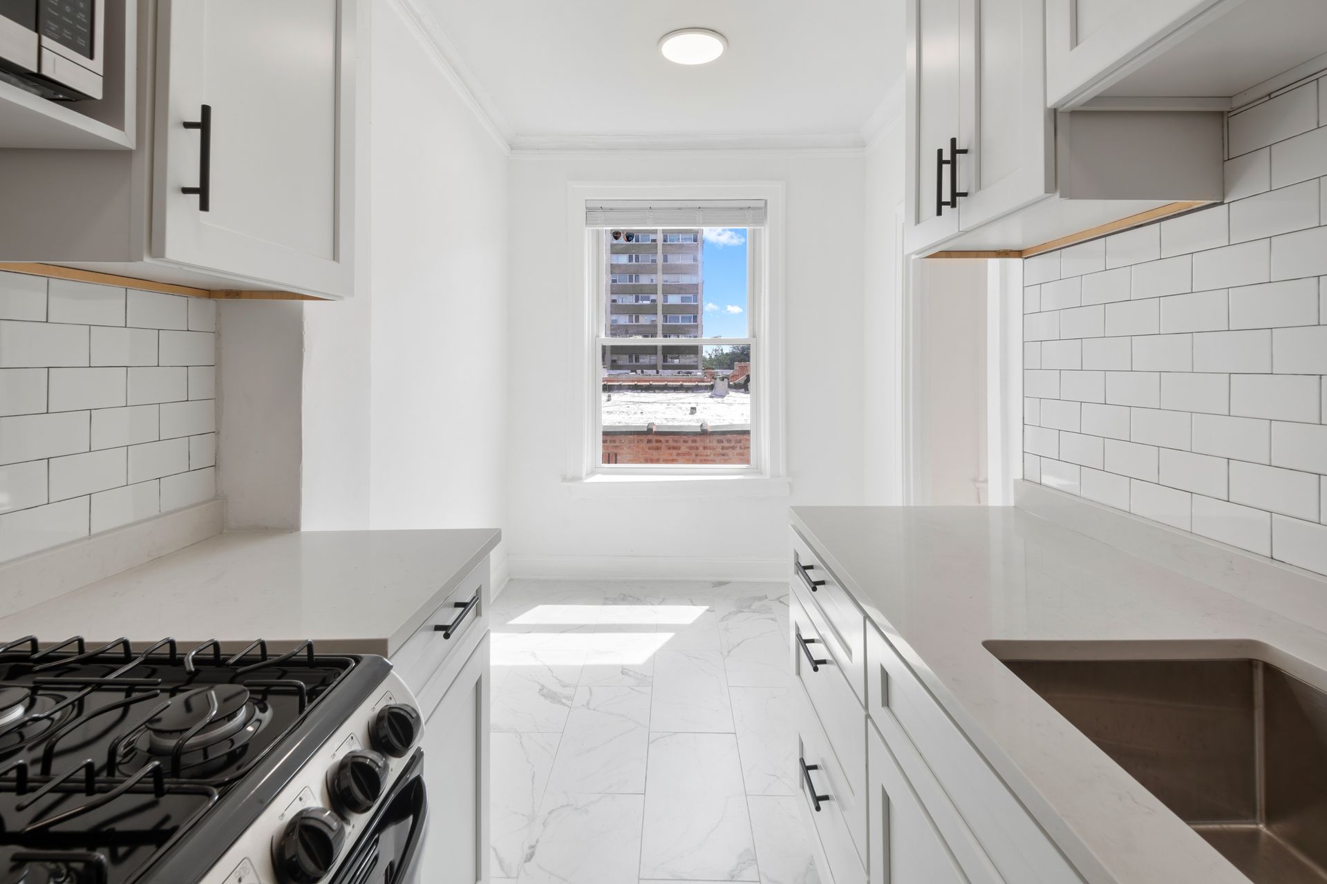 Bright white kitchen with a window and stainless steel sink and stove.