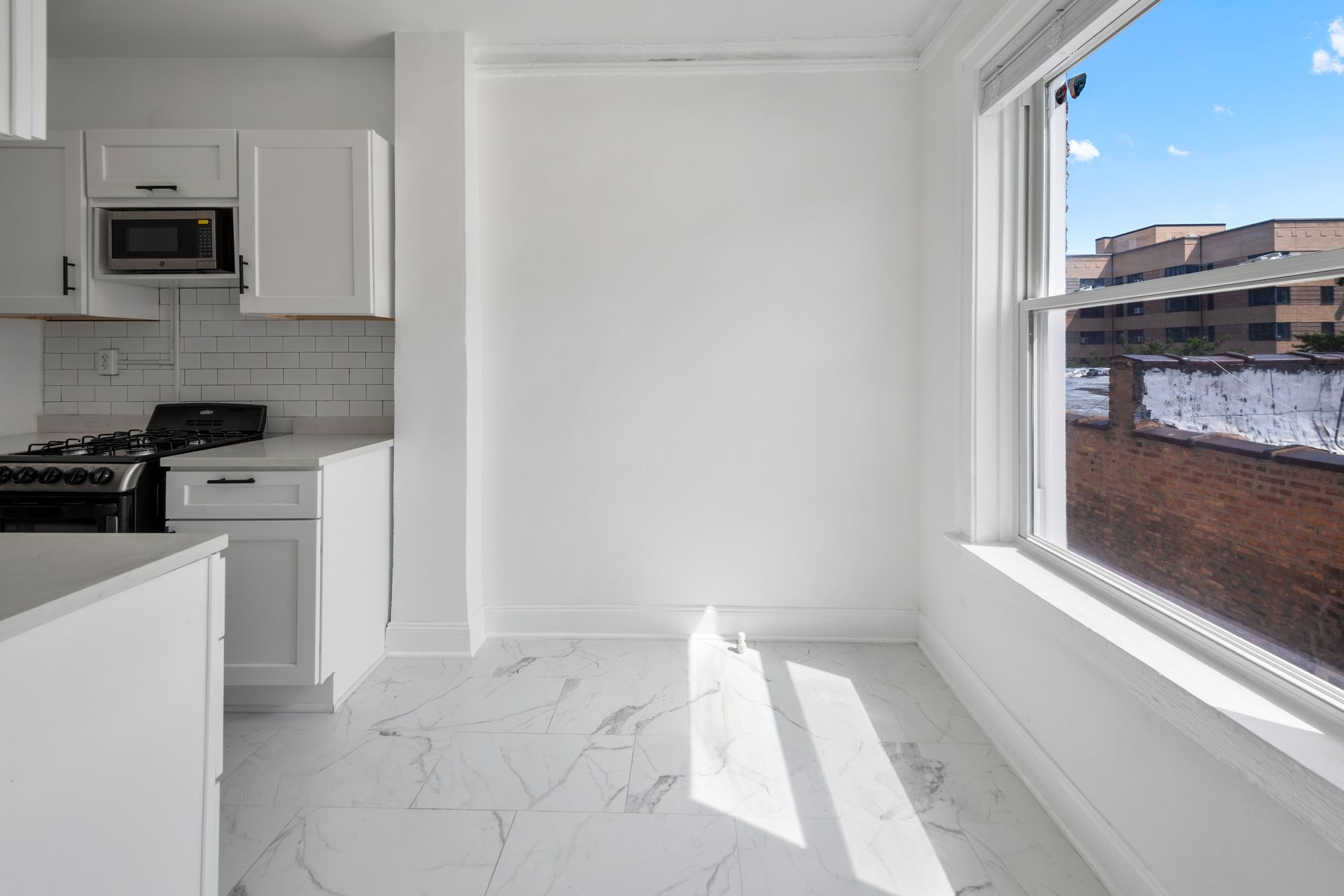White kitchen with black appliances, large window with a view.
