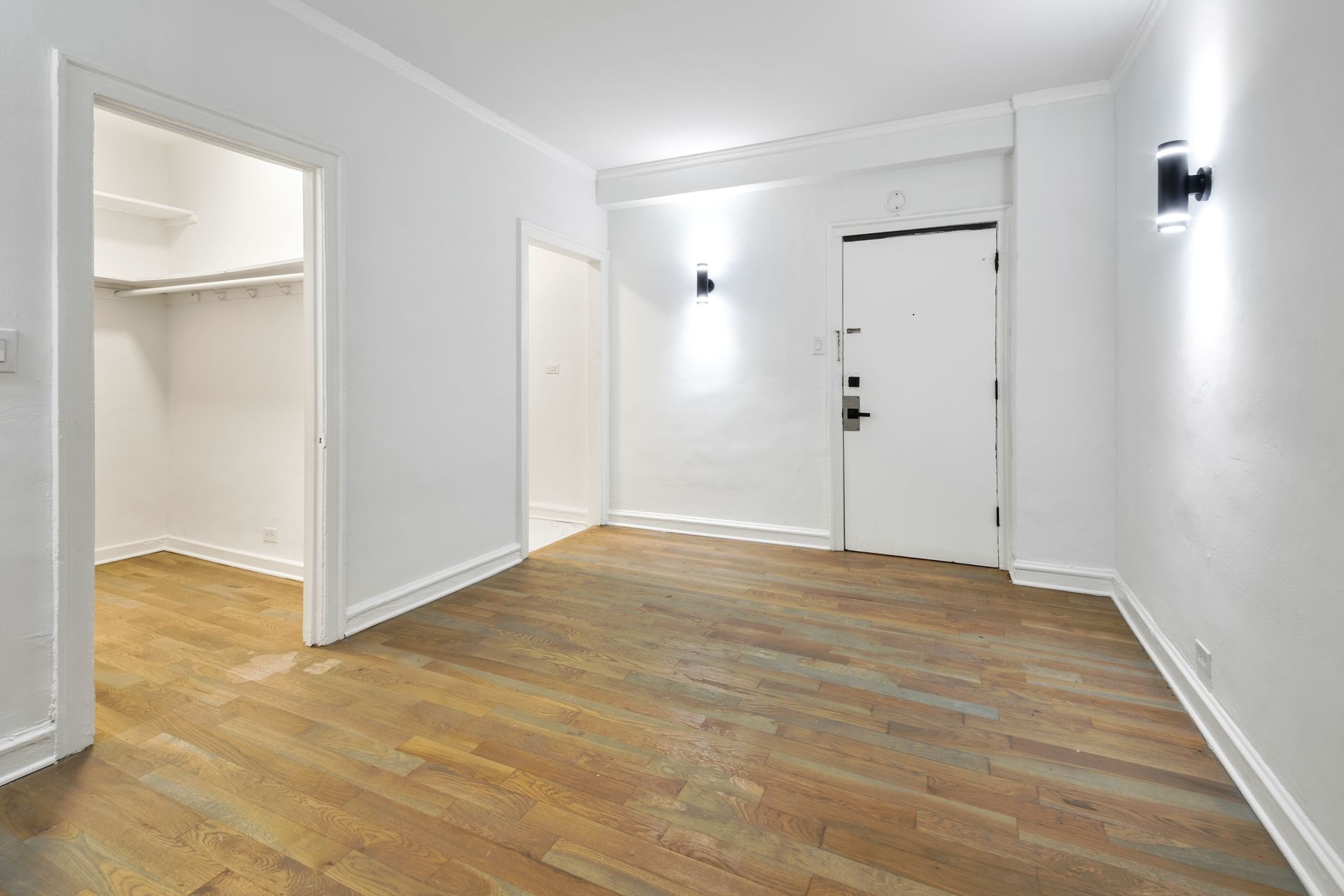 Empty apartment entryway with hardwood floors, white walls, and a closet.
