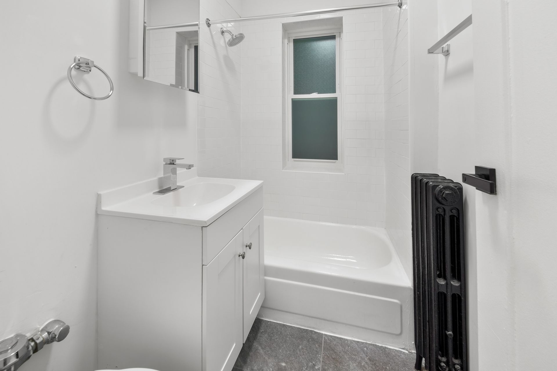 White bathroom with sink, tub, window, and dark radiator.