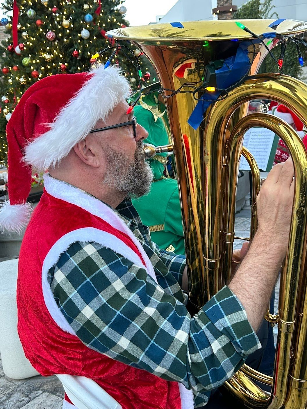 Photo of one of our tuba players at the Christmas concert in 2025 playing his tuba and dressed in a santa vest and hat.