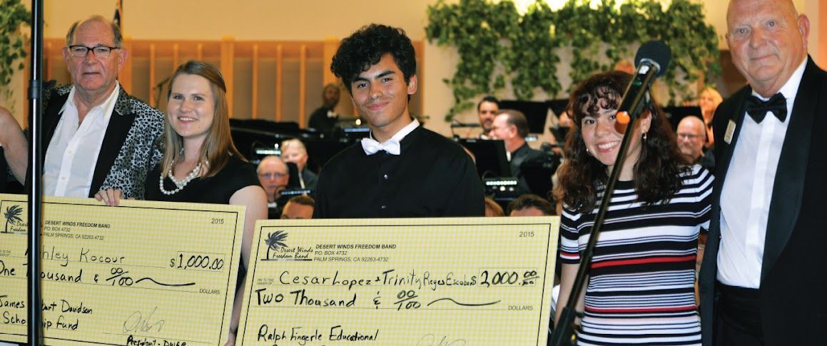 Scholarship winners holding large checks,  with our band in the background.