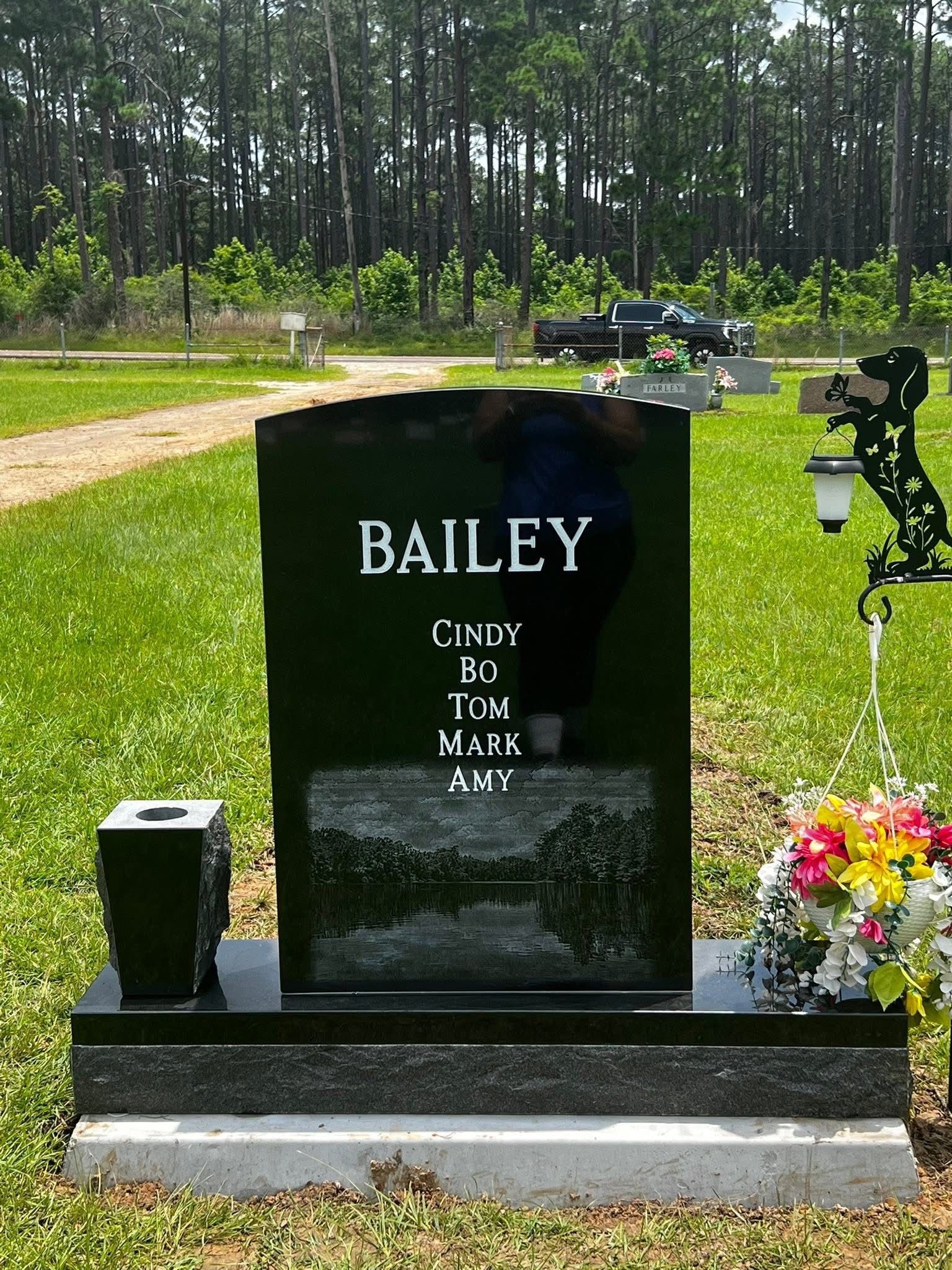 Black Bailey memorial headstone with flowers and ornaments in a cemetery under trees
