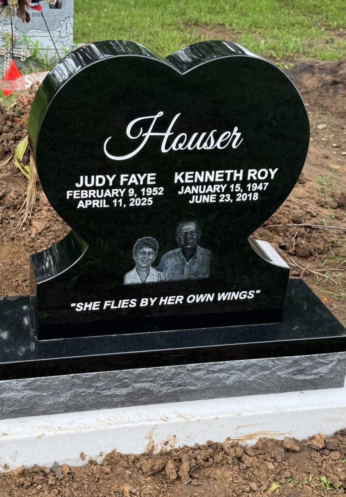 Heart-shaped black granite gravestone with engraved names Judy Faye and Kenneth Roy, in a cemetery.