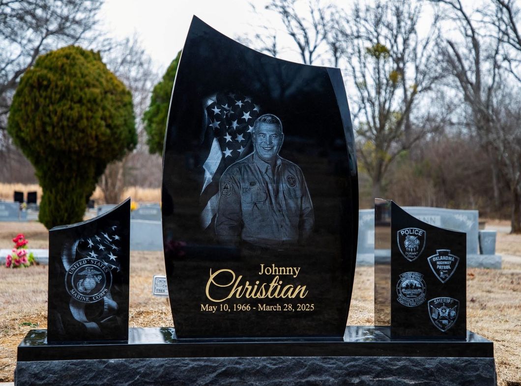 Black granite memorial headstone with engraved portrait and gold lettering in a cemetery yard