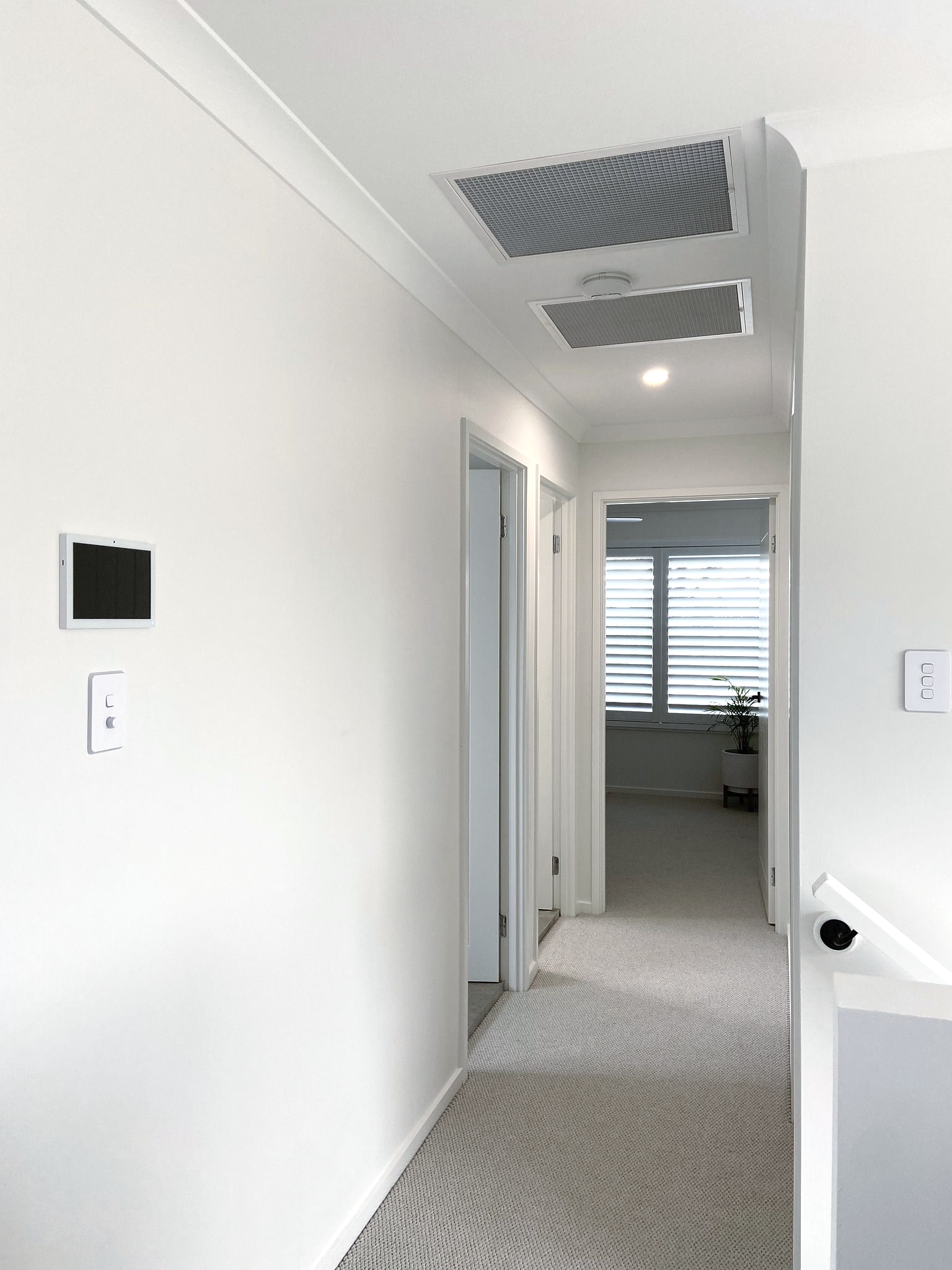 Bright hallway with white walls, carpet, ceiling vents, and an open doorway leading to a windowed room — JF Air Conditioning Pty Ltd in Edgeworth, NSW