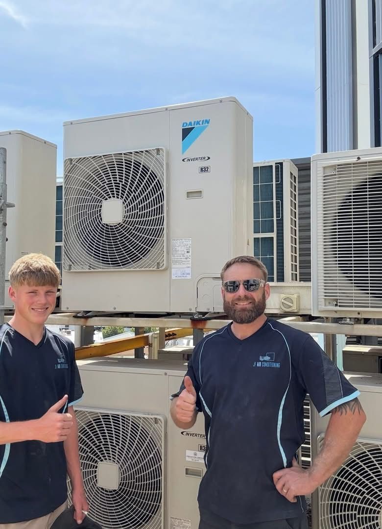 Two people giving thumbs up beside large outdoor cooling units under a blue sky — JF Air Conditioning Pty Ltd in Edgeworth, NSW