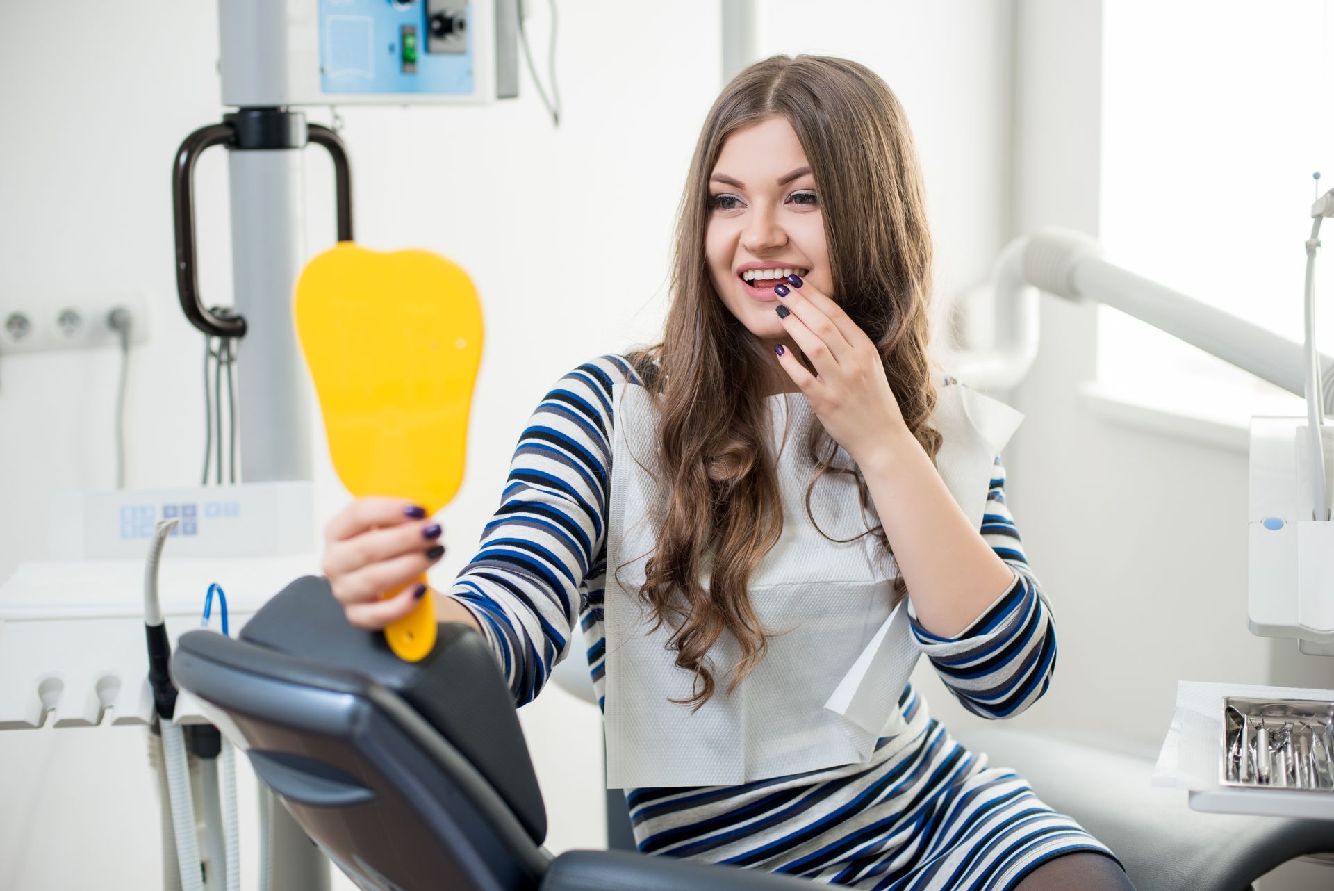 A dentist adjusts a patient’s head as they hold a mirror during a dental checkup. A patient with perfect white teeth sitting in a dental chair, checking her teeth after a smile.