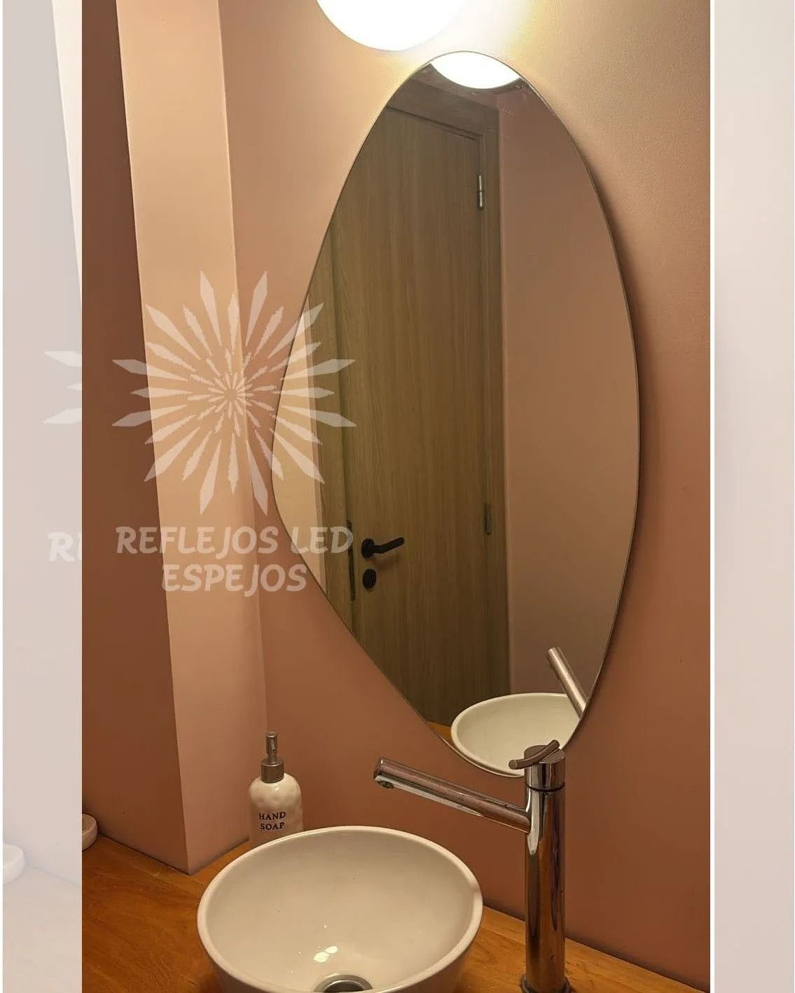 Lavabo moderno con espejo ovalado y paredes color beige, que deja ver una pila blanca y un grifo cromado.