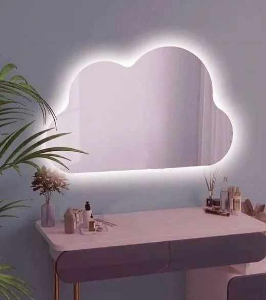 Tocador minimalista con espejo luminoso en forma de nube, iluminación rosa suave y pequeños objetos decorativos.