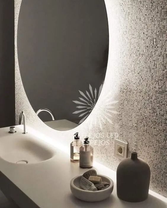 Tocador de baño moderno con espejo ovalado, lavabo, dispensadores de jabón y decoración de pared texturizada.