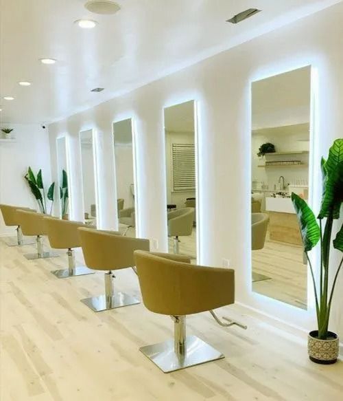 Salón de belleza moderno con sillones de peluquería color canela, espejos altos, paredes blancas y suelo de madera clara.