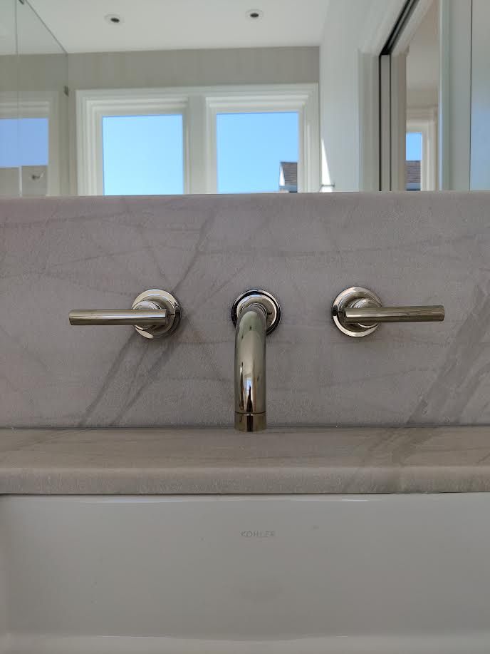 Chrome bathroom faucet on a marble sink beneath a large mirror and window.