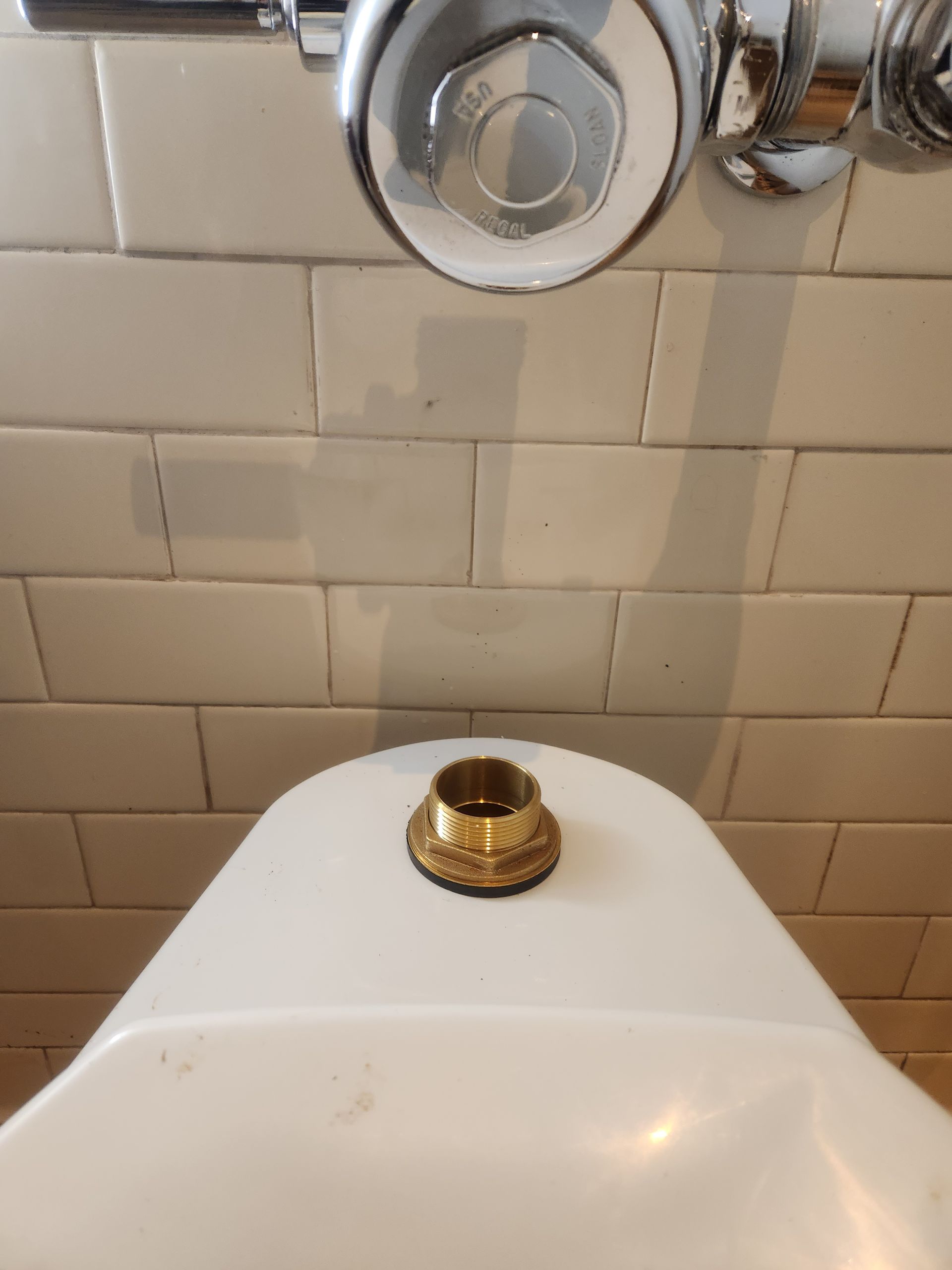 Close-up of a bathroom sink with a gold faucet fixture and beige tiled wall behind it