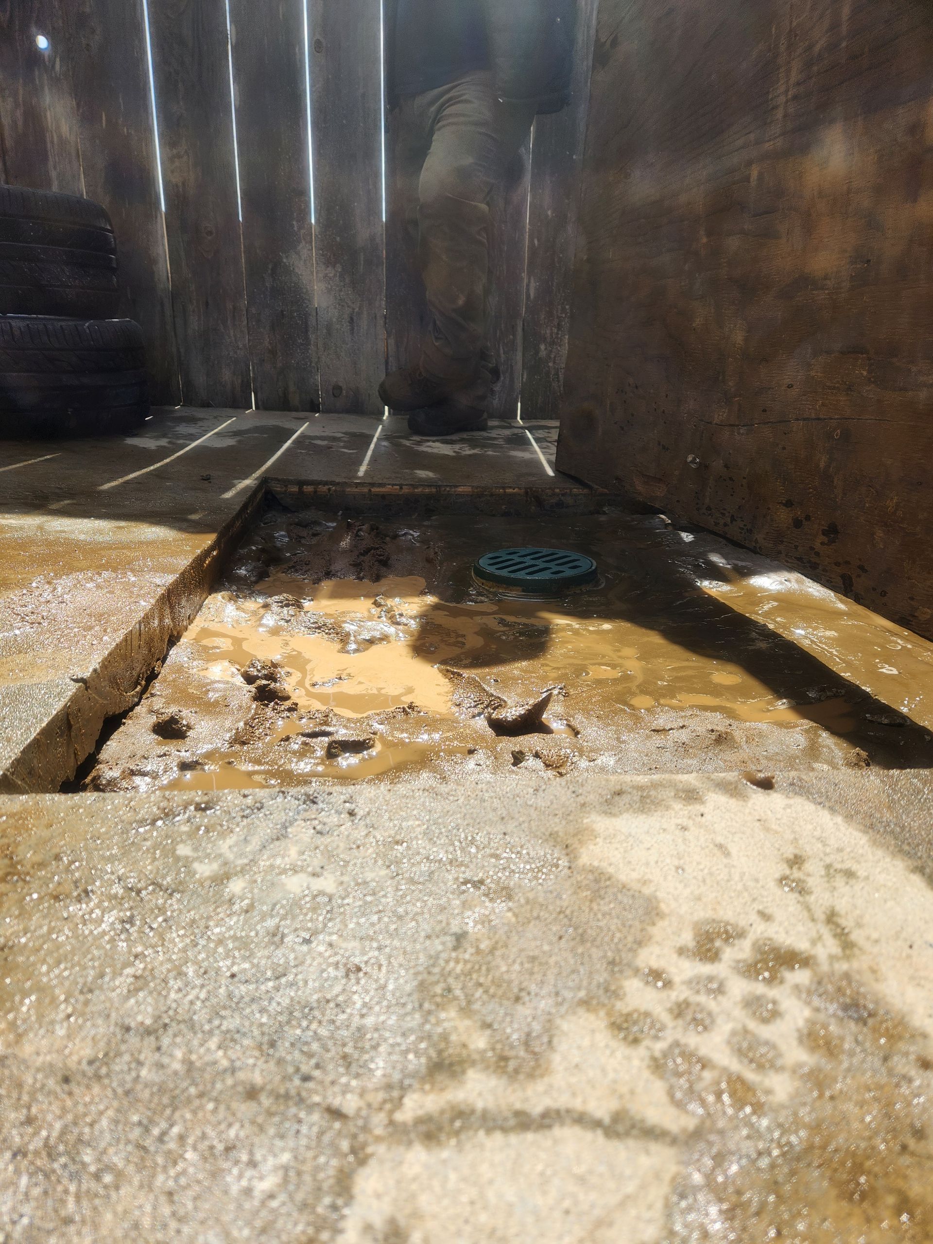 Dirty concrete sink area with a drain, standing water, and wet stains against dark walls