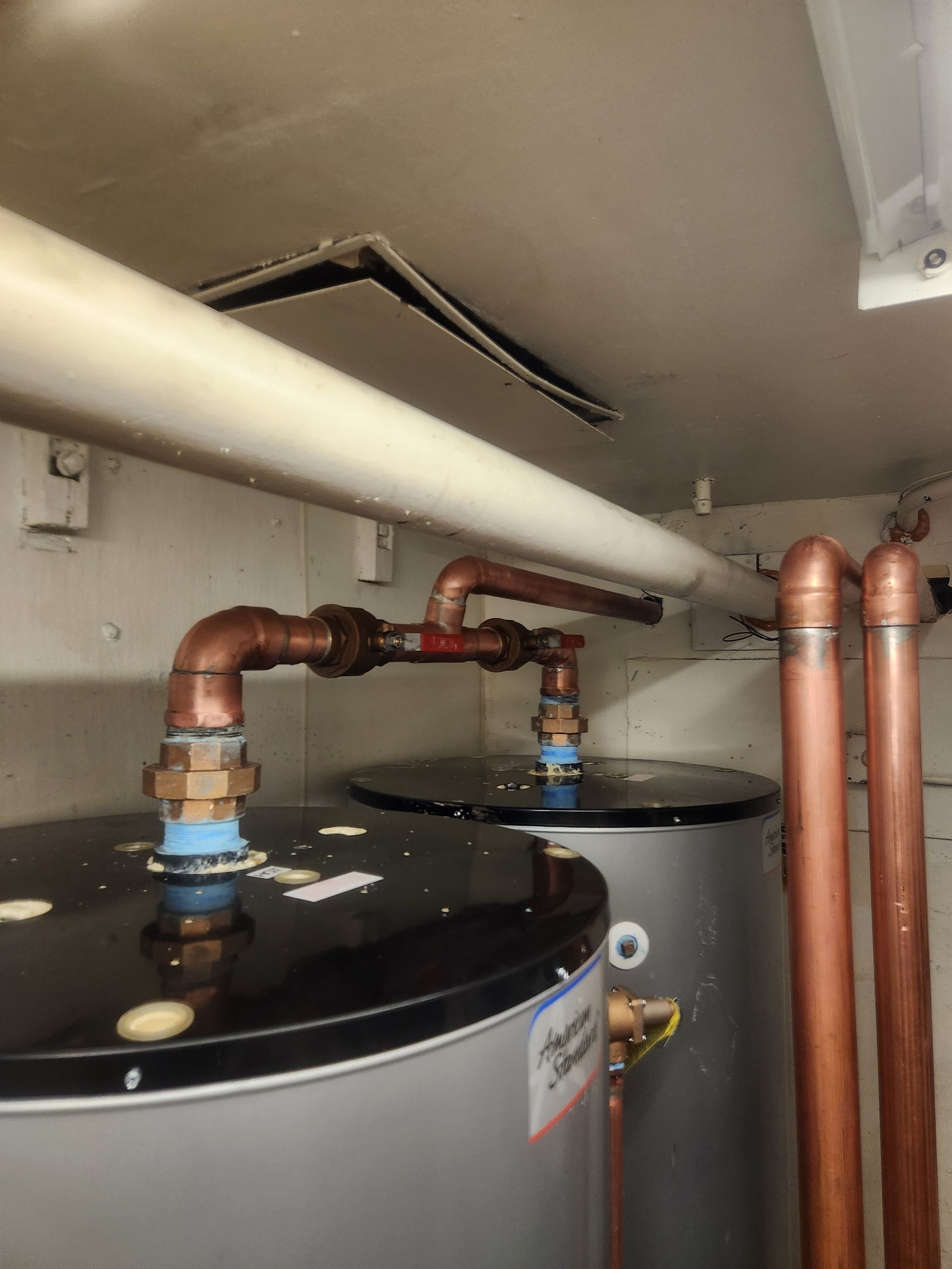 Water heater pipes and tanks in a cramped utility closet with a damaged ceiling panel above