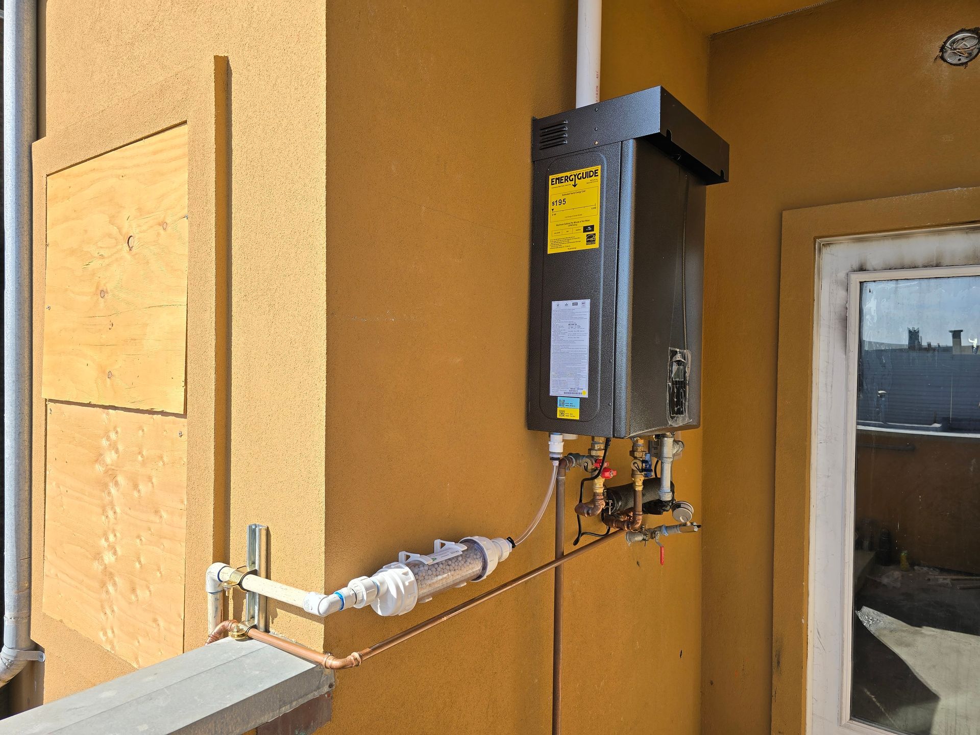 Gray electrical meter and conduit mounted on an orange exterior wall near a window.