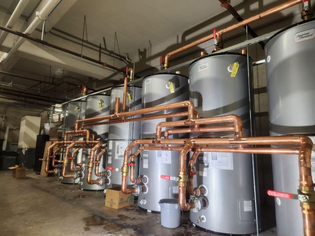 Industrial plant room with large gray tanks and copper pipes along a concrete floor