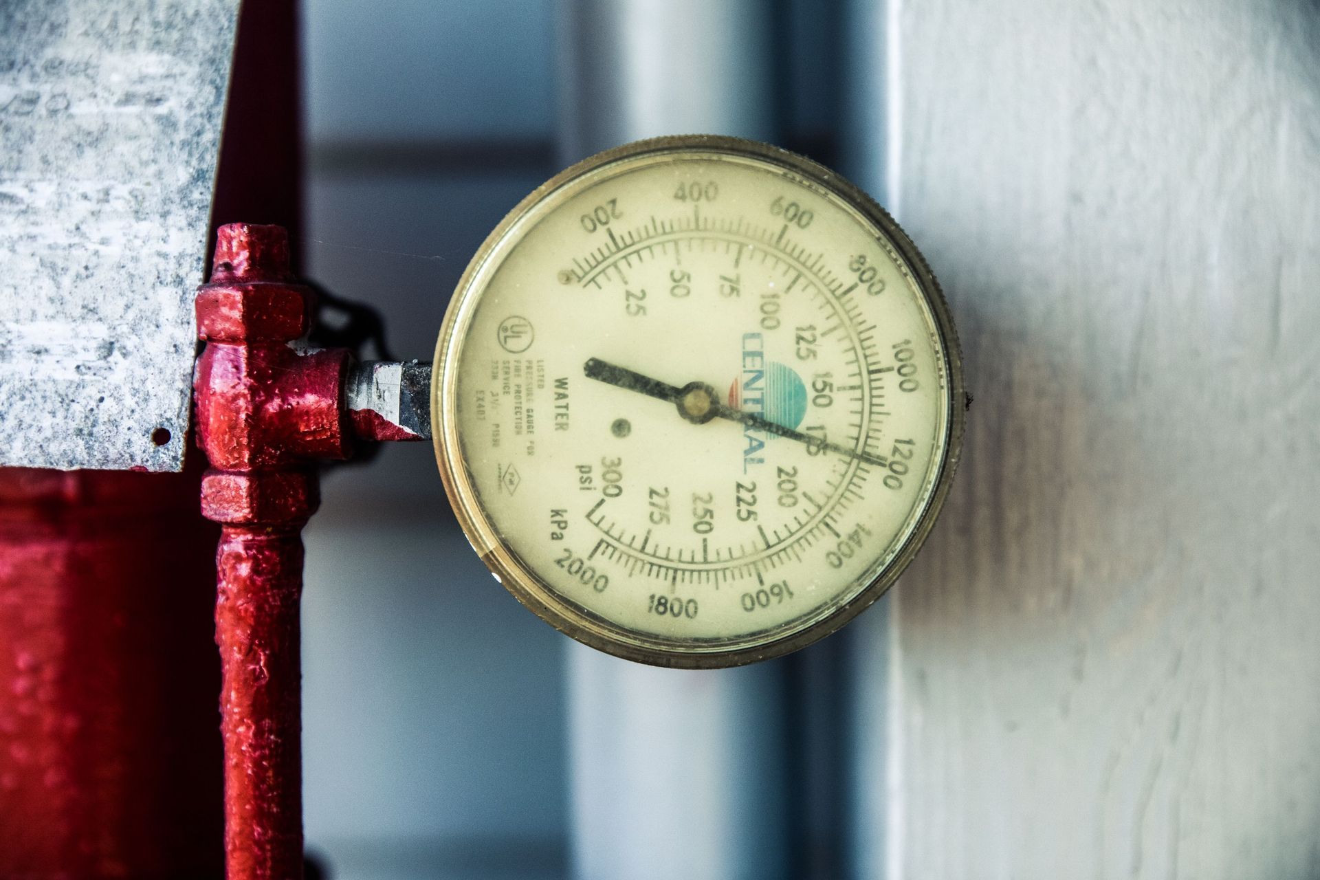Round pressure gauge on a red pipe against a blurred industrial background.