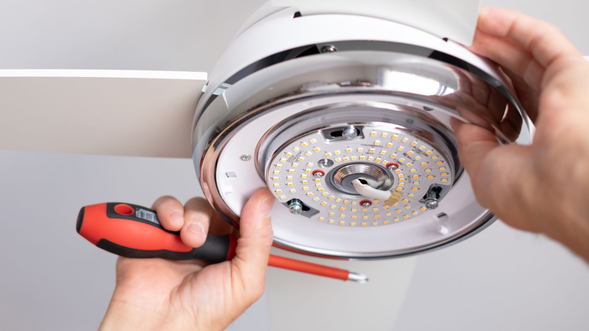 A person is fixing a ceiling fan with a screwdriver.