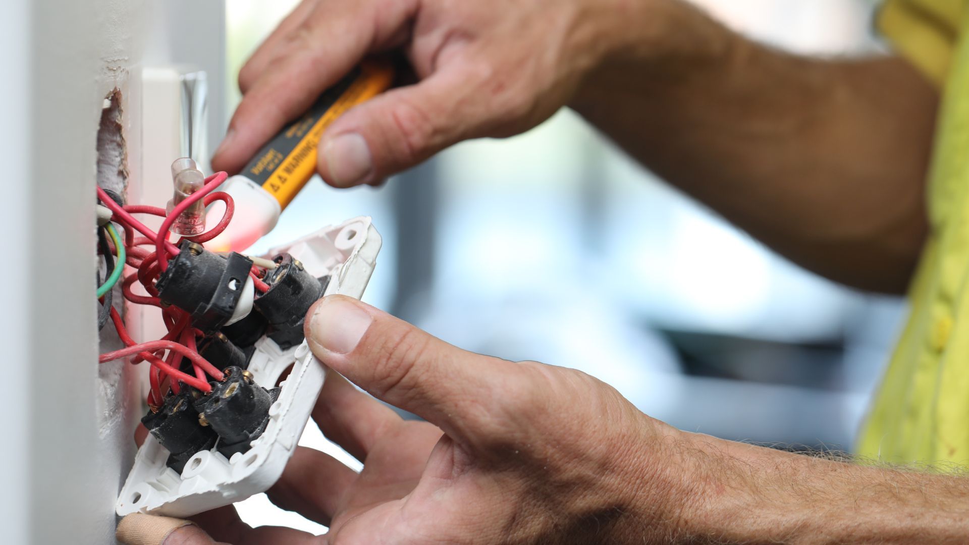 A man is working on a light switch with a screwdriver.