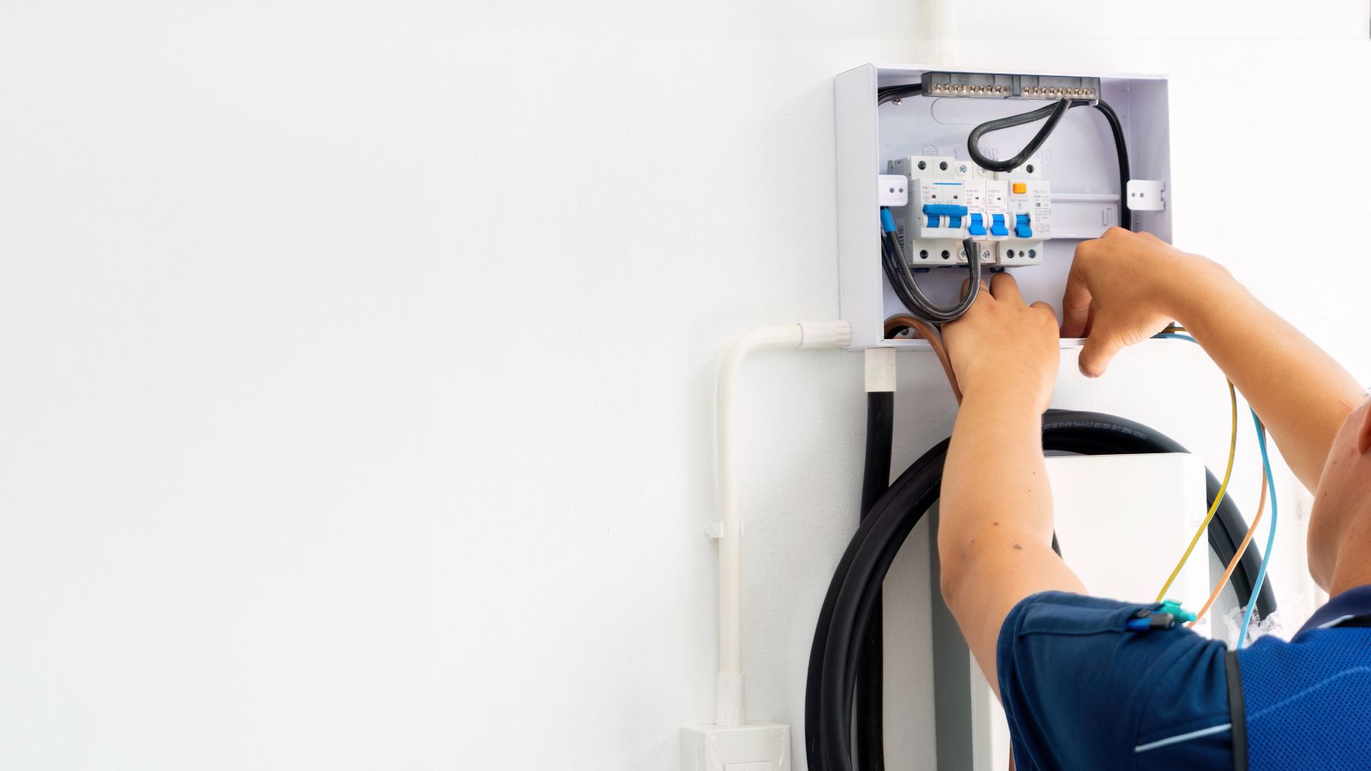 A man is working on an electrical box on a wall.