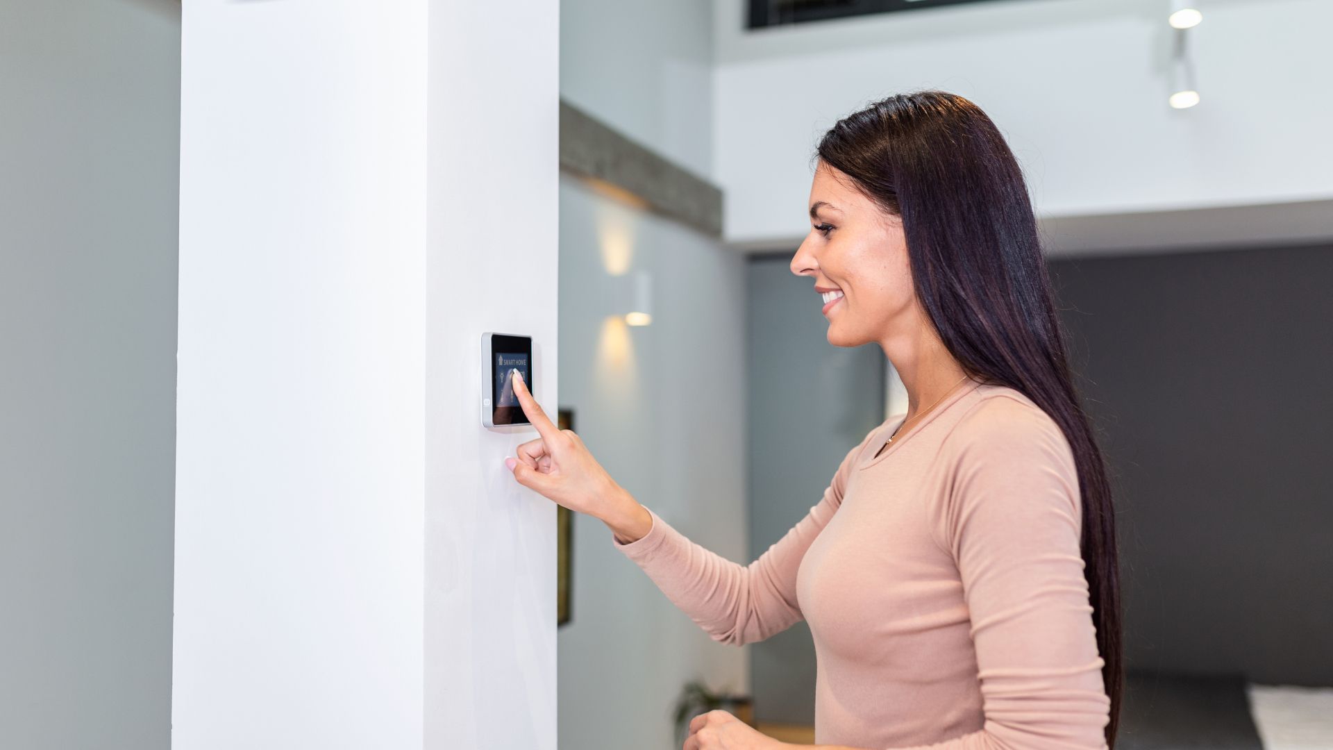 A woman is using a smart thermostat in her home.
