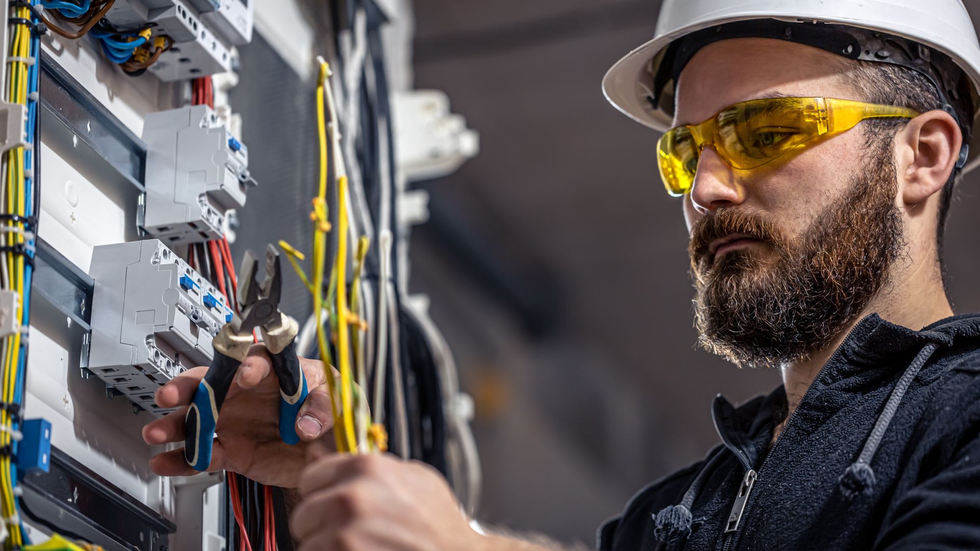 A man wearing safety glasses and a hard hat is working on an electrical box.