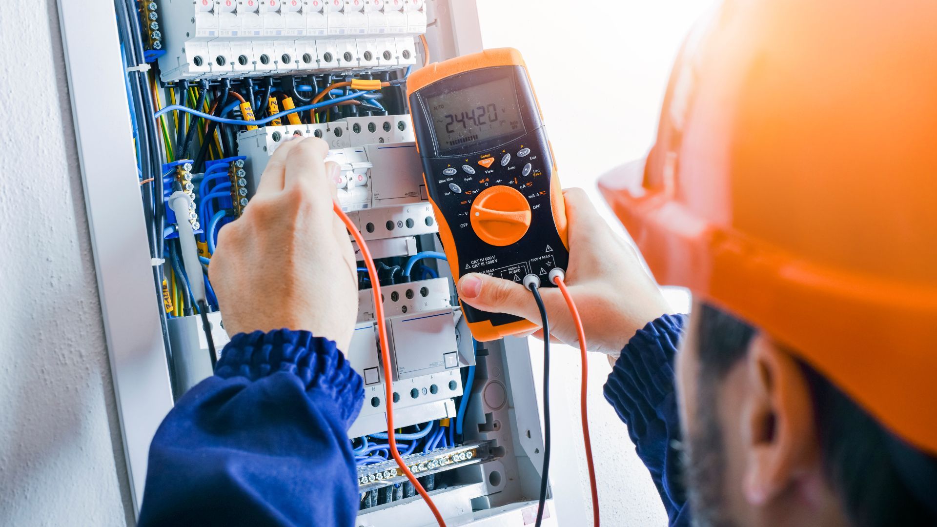An electrician is working on an electrical box with a multimeter.