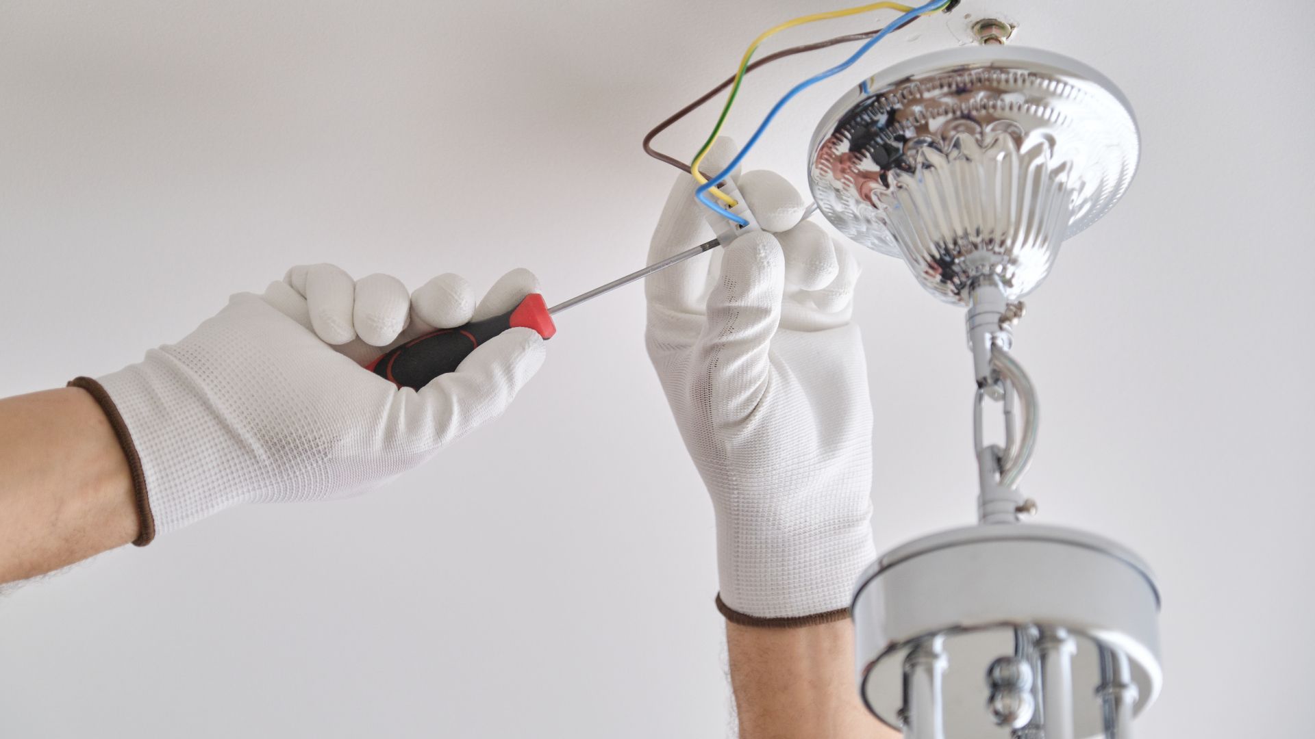 A person is fixing a light fixture with a screwdriver.