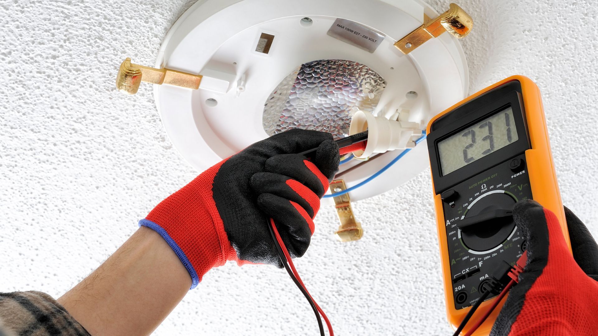 A person is using a multimeter to test a smoke detector.