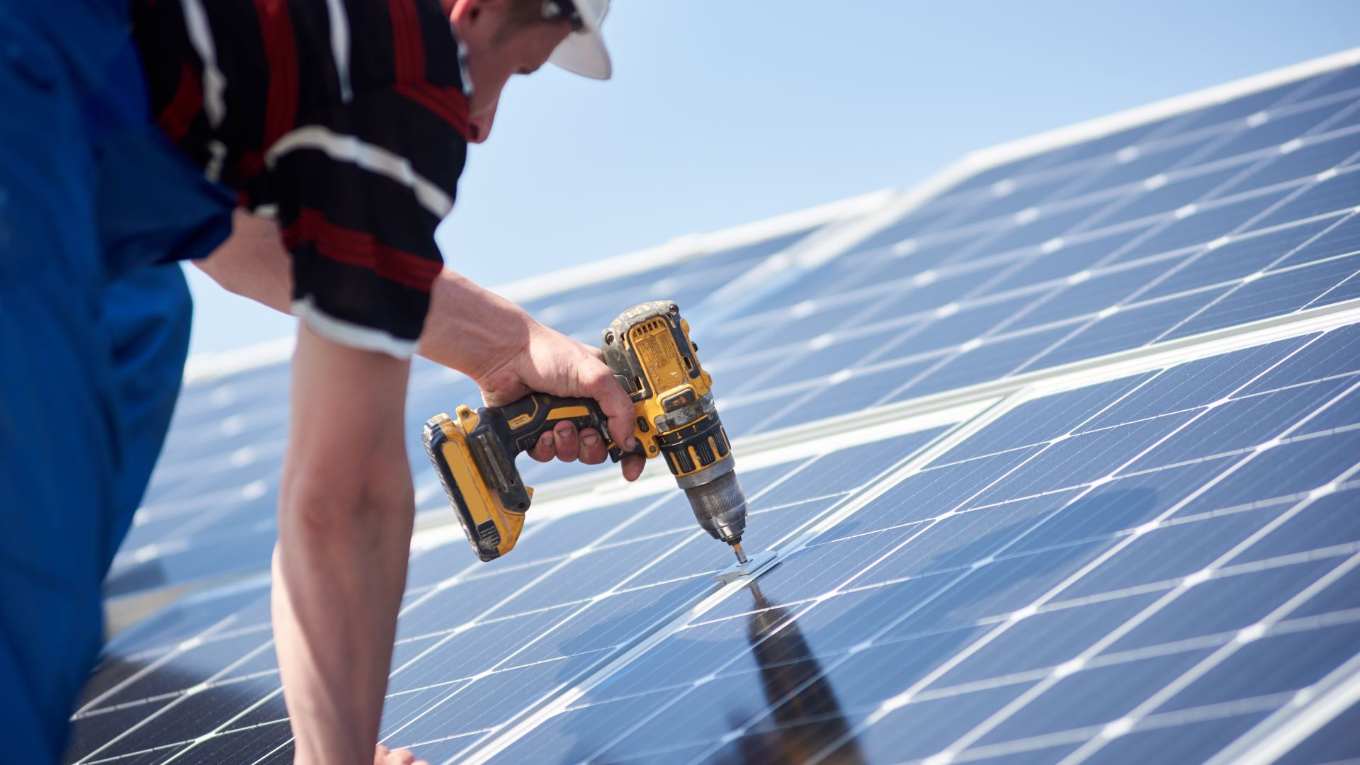 A man is installing solar panels on a roof with a drill.