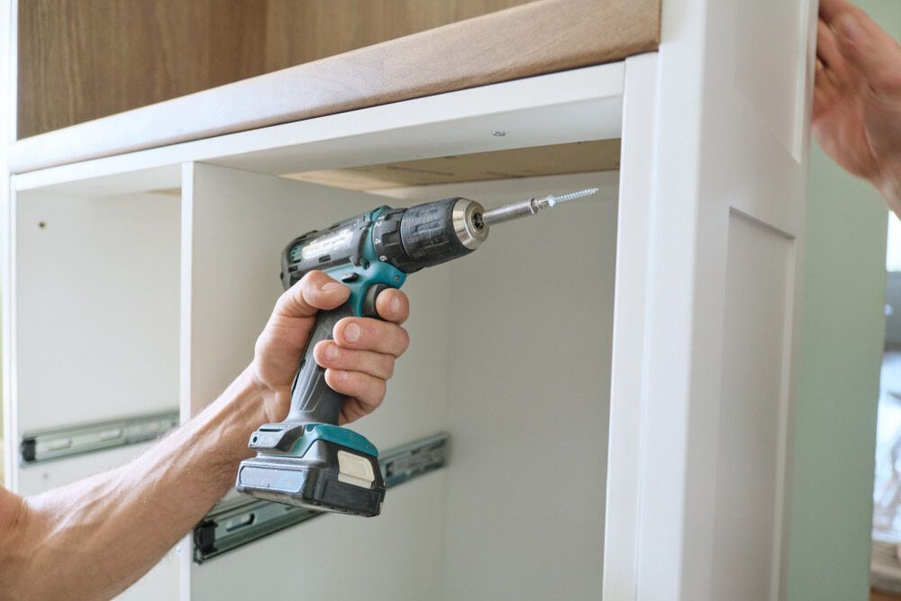 A man is using a cordless drill to install a cabinet — Mark's Flooring & Handyman Services in Tuggerah, NSW