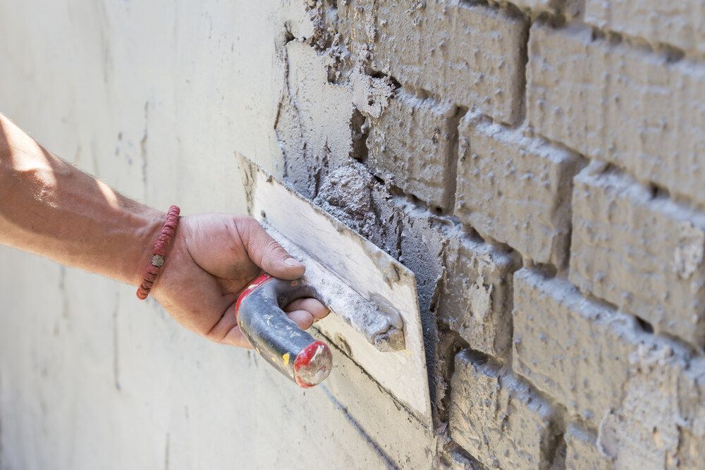 A Person is Plastering a Brick Wall With a Trowel — Mark's Flooring & Handyman Services in Tuggerah, NSW