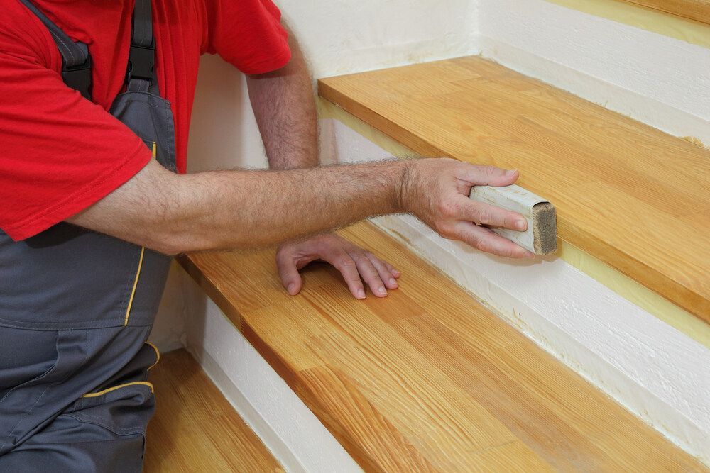 A Man is Sanding a Wooden Staircase With a Sander — Mark's Flooring & Handyman Services in The Entrance, NSW