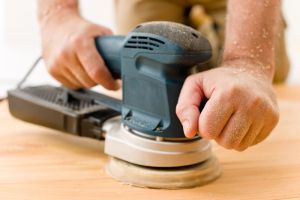 A Person is Sanding a Wooden Surface With a Sander — Mark's Flooring & Handyman Services in Chittaway Bay, NSW