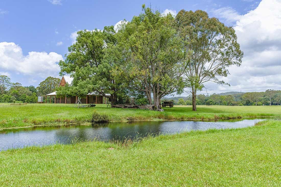 A House is Sitting in the Middle of a Grassy Field Next to a River — Mark's Flooring & Handyman Services in Ourimbah, NSW