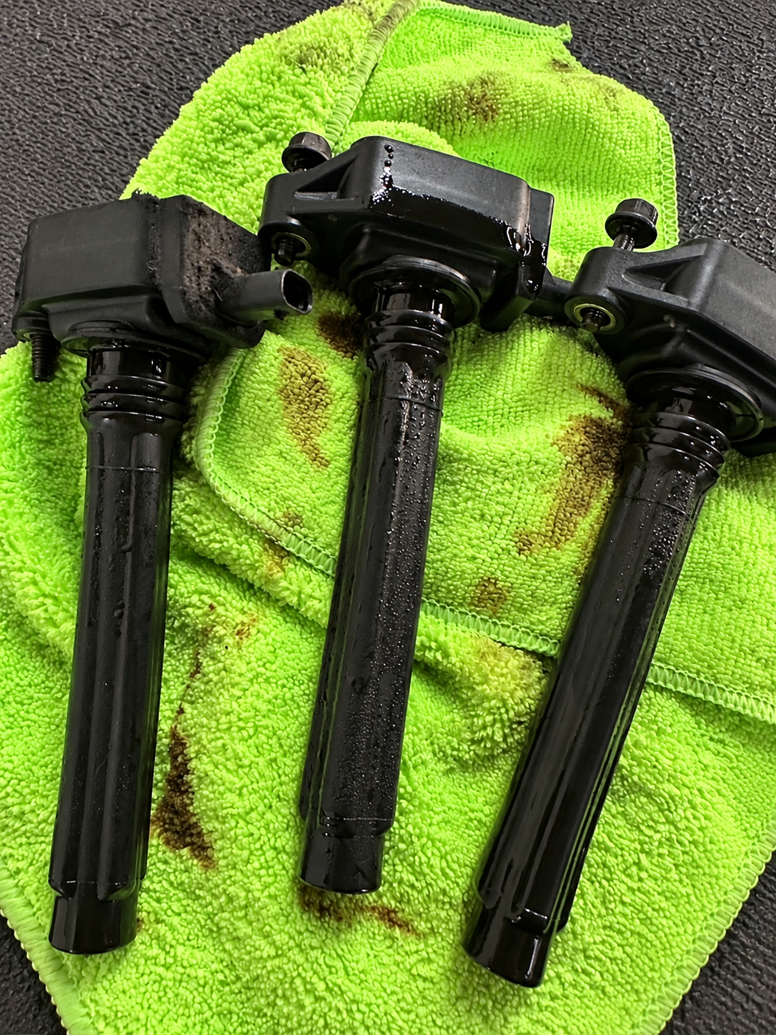 Three oily ignition coils on a green shop towel