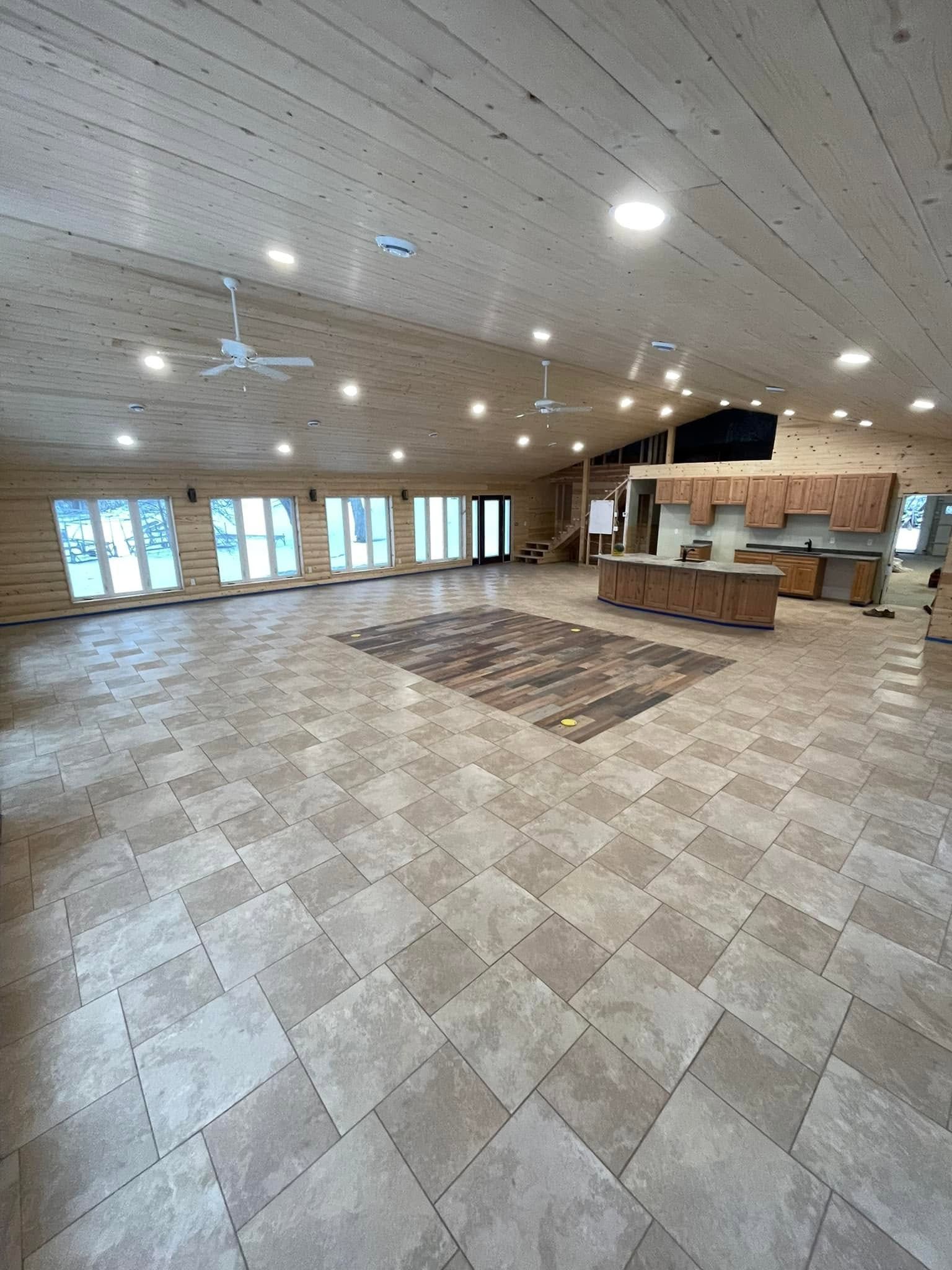 Spacious empty hall with tiled floor, wood-paneled ceiling, and rows of windows along the wall.