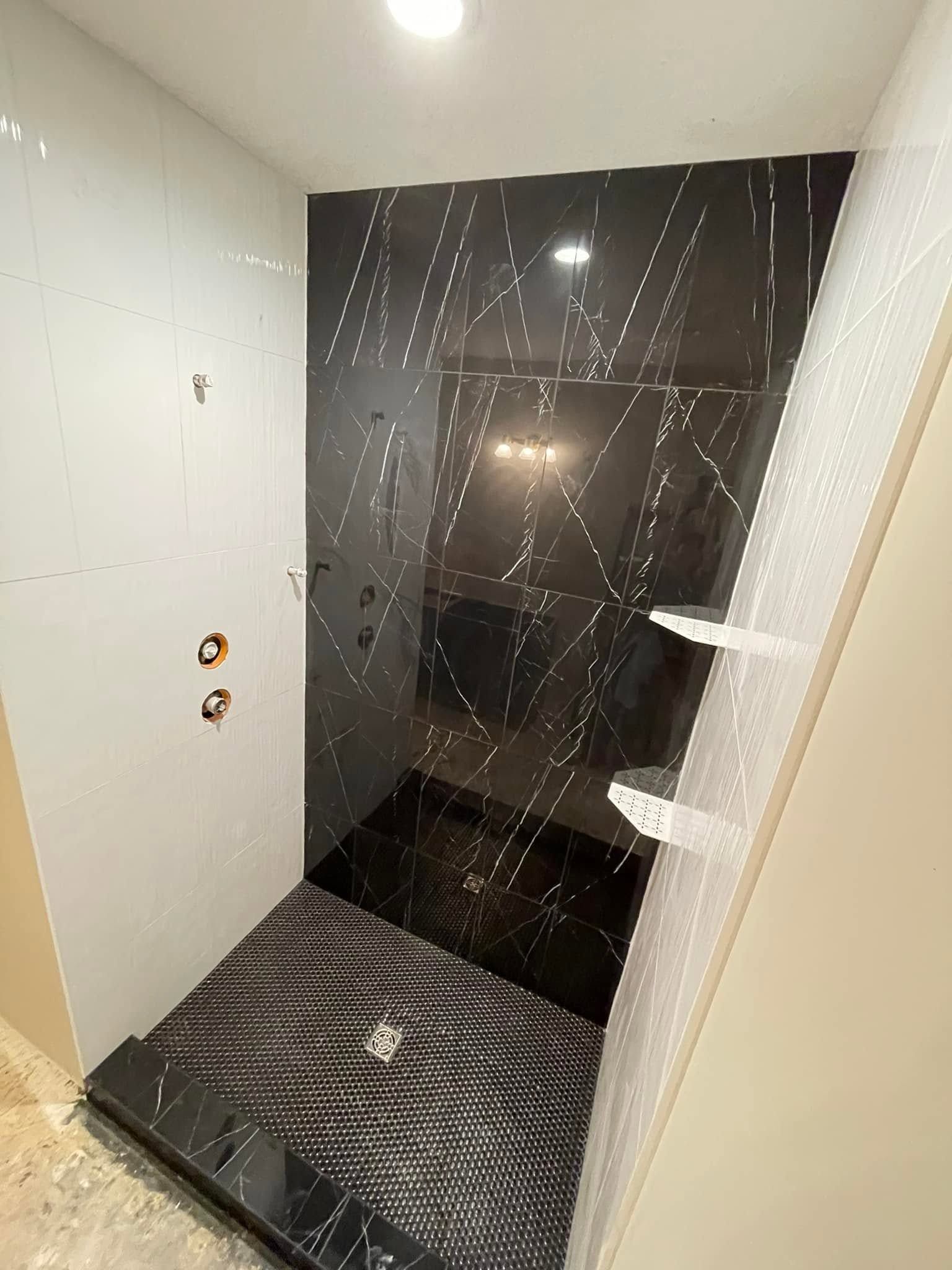 Small shower stall with black glass door, white tiled walls, and dark tiled floor.